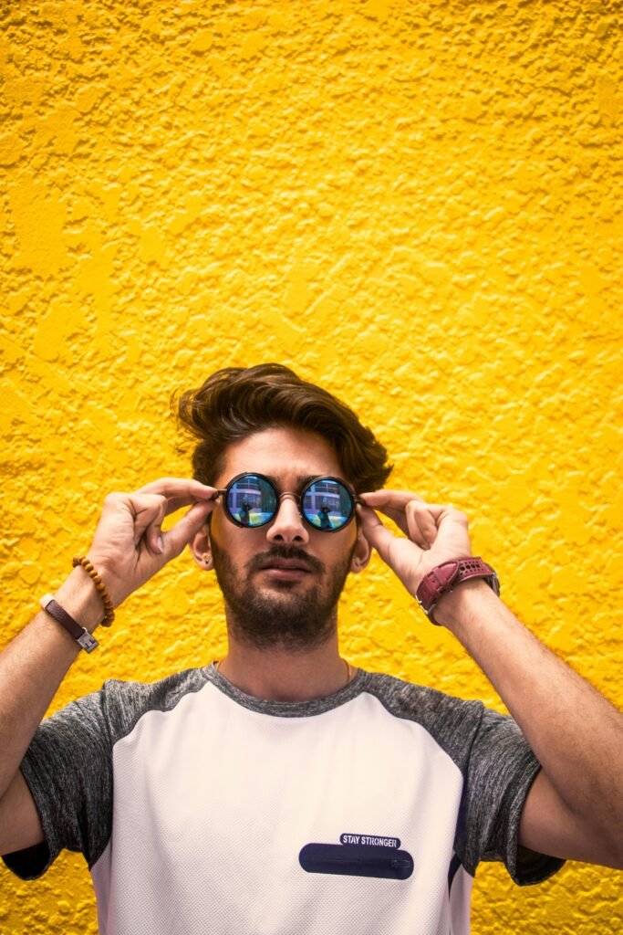 Man in White and Gray Shirt Wearing Sunglasses Against Yellow Wall